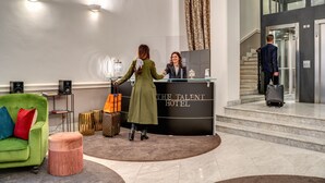 Zona de recepción de un hotel con un sofá verde, un otoman rosa y un mostrador de recepción.