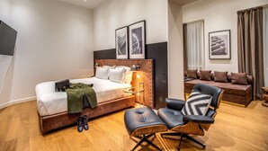 Una habitación de hotel moderna con una cama grande, un área de descanso con un sofá y sillones, y obras de arte en las paredes.