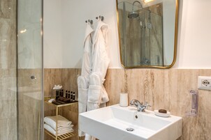 A modern bathroom with a glass shower enclosure, a white sink with a gold faucet, and a marble-tiled wall.