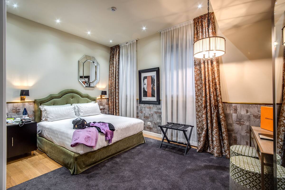 Una habitación de hotel con una cama grande, un escritorio y una silla. Hay un espejo en la pared y un marco de cuadros.