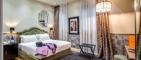 Une chambre d’hôtel avec un grand lit, un bureau et une chaise. Il y a un miroir au mur et un cadre photo.