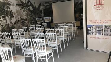 Une salle de conférence avec des chaises blanches disposées en rangées, un écran de projection et une banderole ornée du logo de BuildInvest.