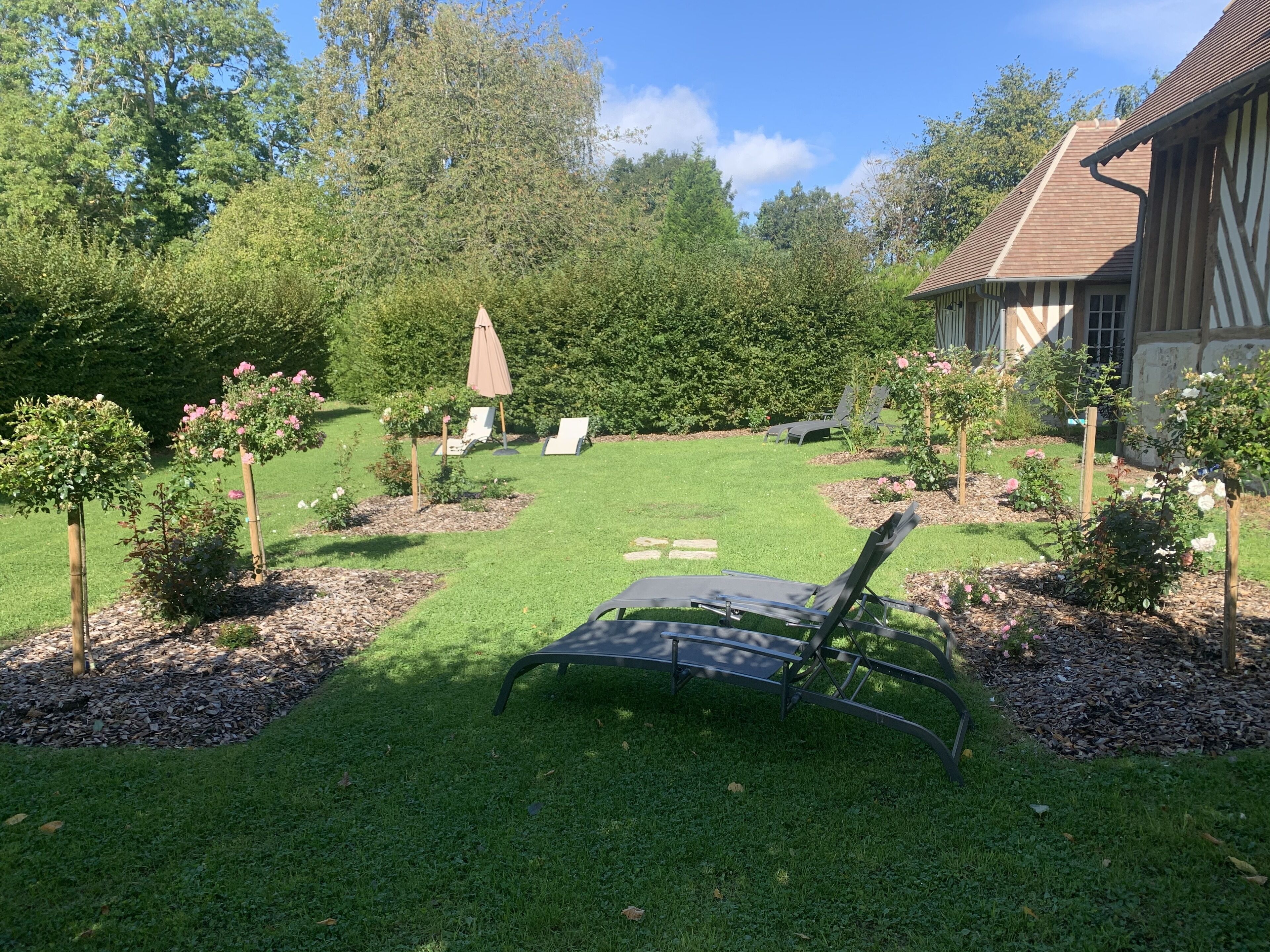 A well-maintained garden with a lawn, a few chairs, and a building with a sloped roof.