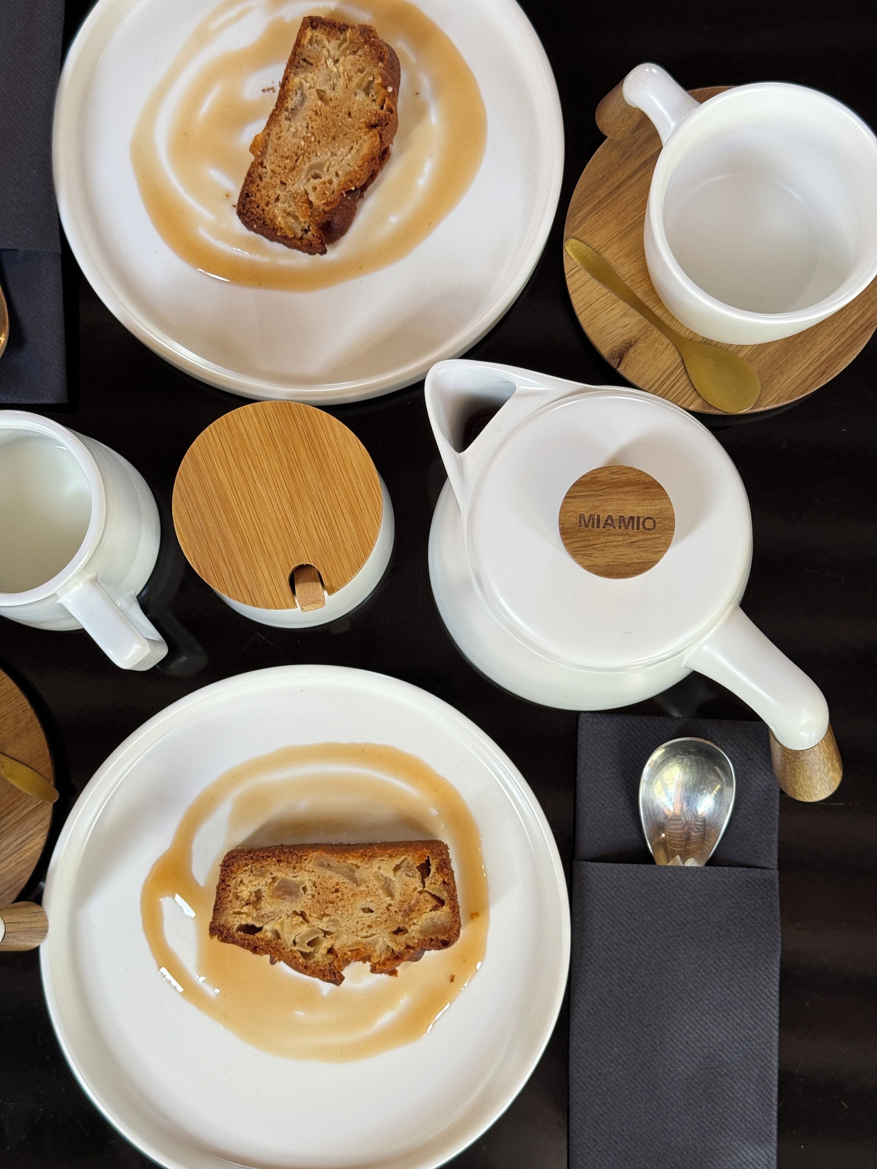 A table set with white plates, a white mug, a white teapot, and a wooden spoon.