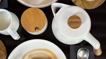 A table set with white plates, a white mug, a white teapot, and a wooden spoon.