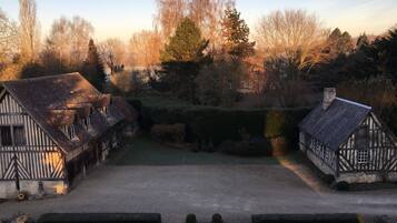 A traditional half-timbered house with a gravel path leading to a small pond, surrounded by trees and hedges.