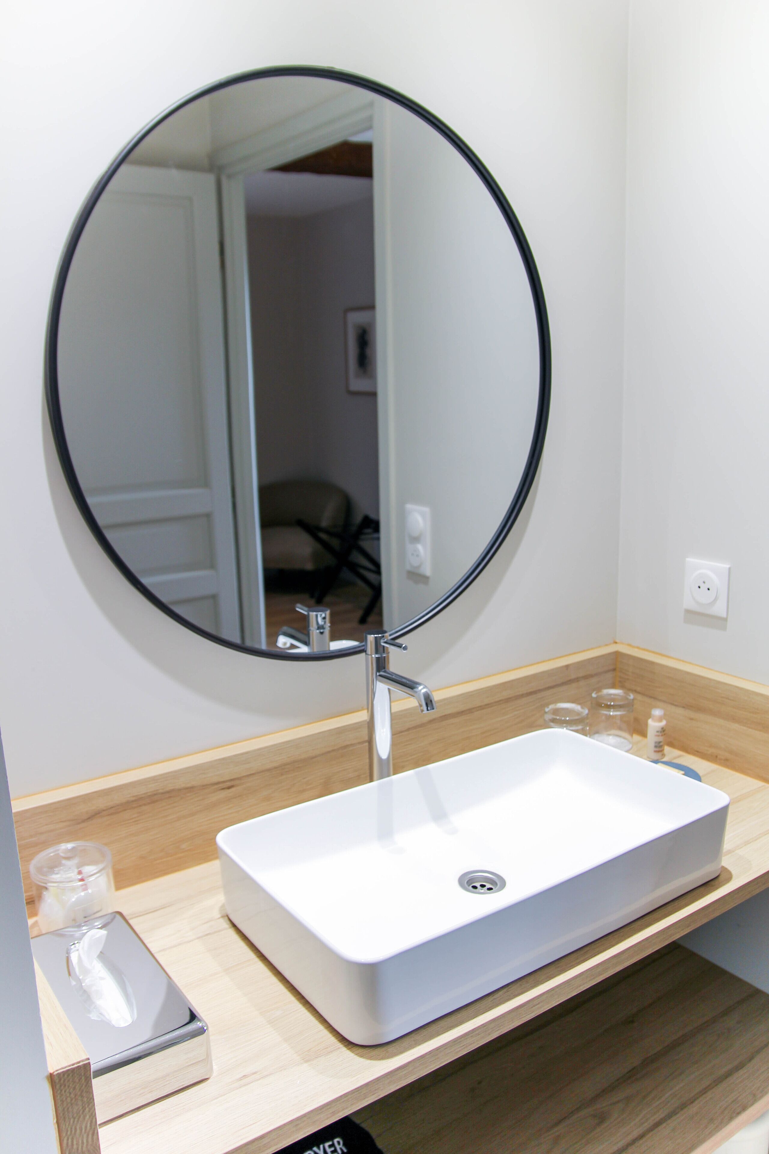 A bathroom with a white sink, a round mirror, and a wooden countertop.