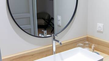 A bathroom with a white sink, a round mirror, and a wooden countertop.