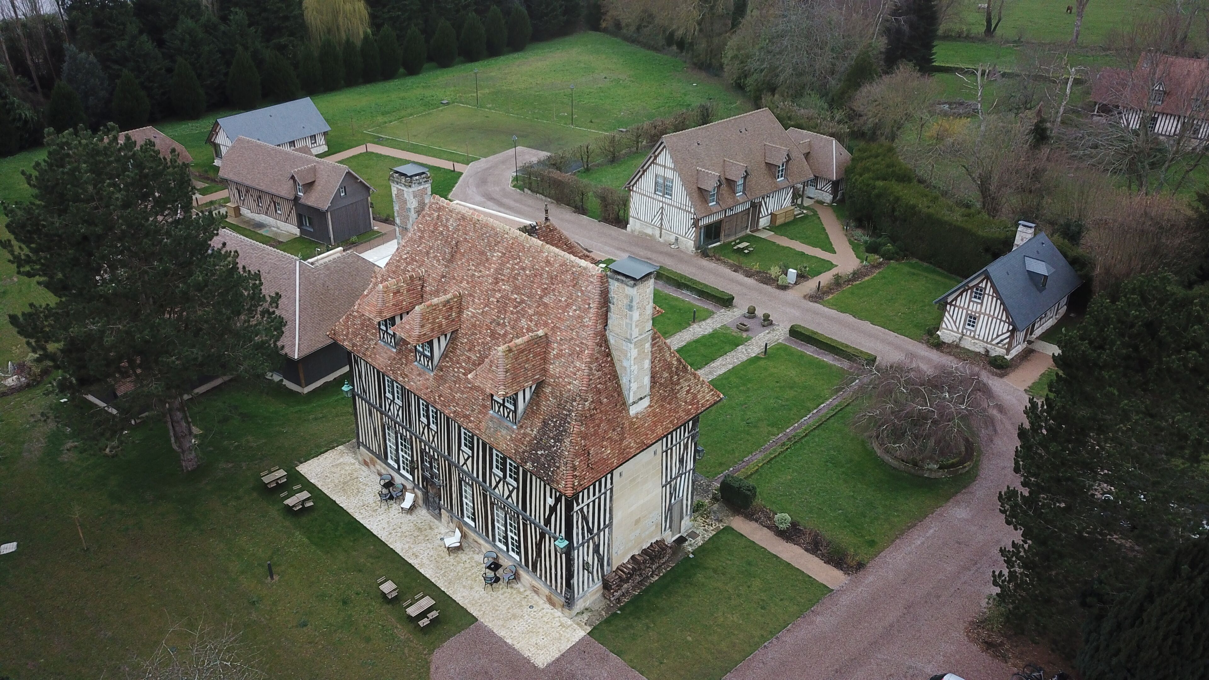 An aerial view of a traditional half-timbered house with a large garden, a tennis court, and a stone tower.