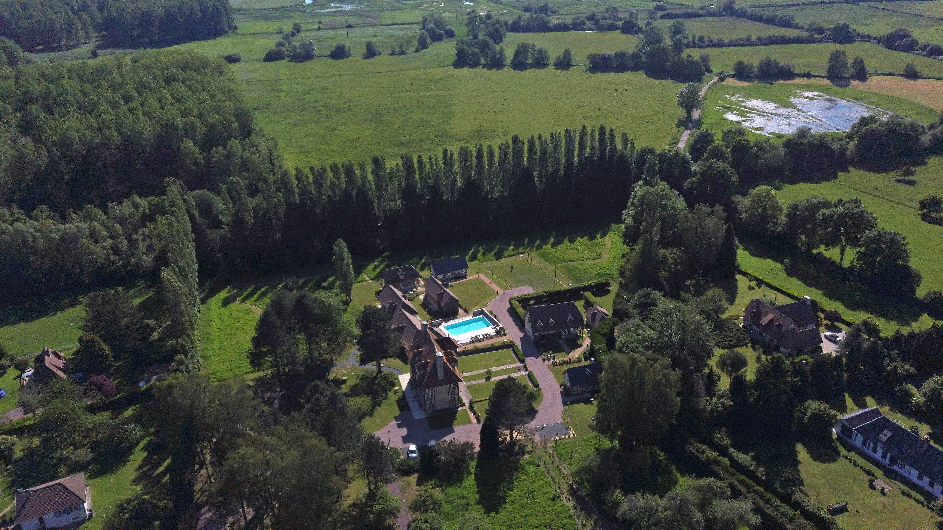 An aerial view of a large estate with a swimming pool, multiple buildings, and extensive green fields.