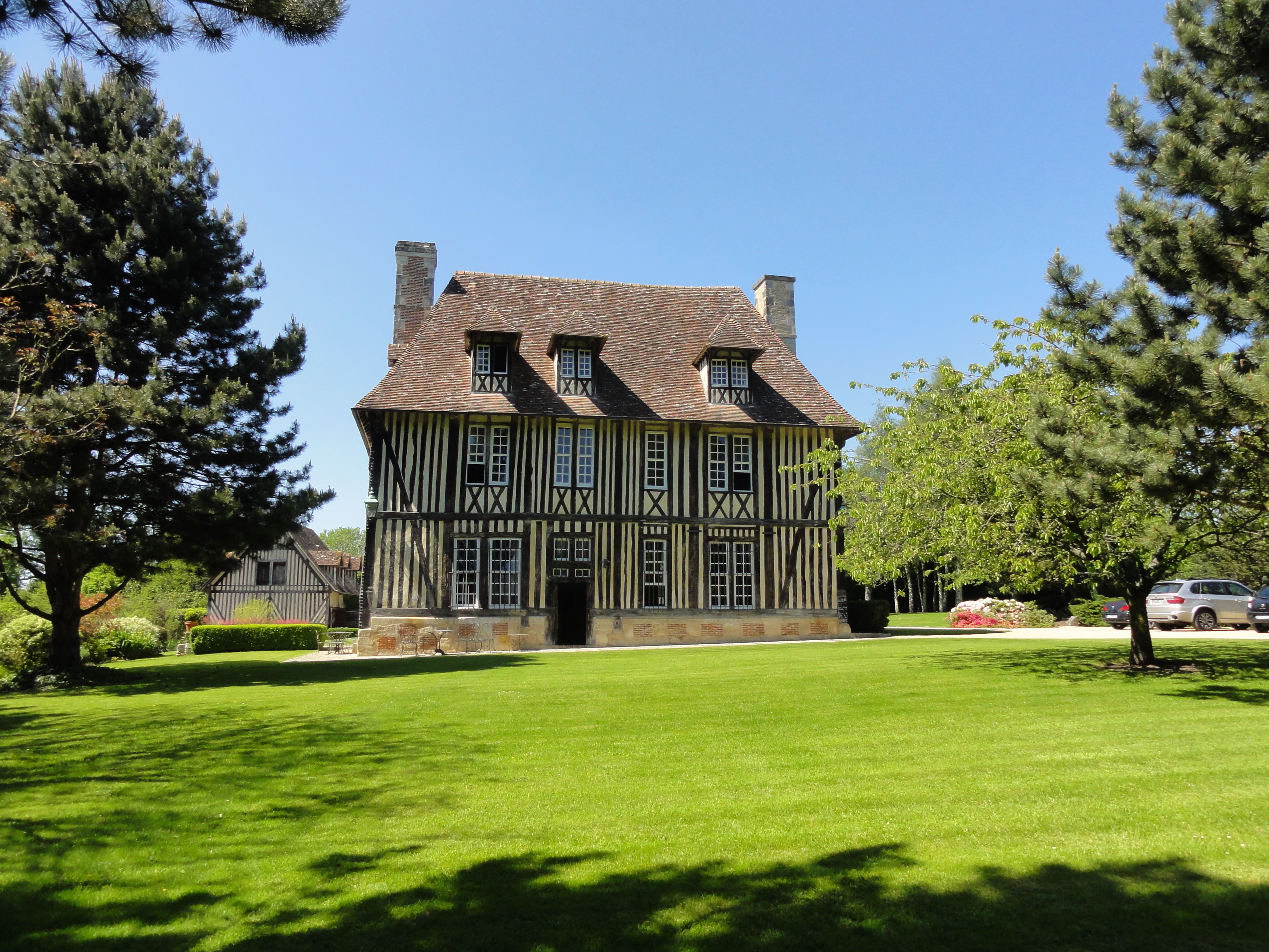 A large, two-story Tudor-style house with a steeply pitched roof, multiple chimneys, and a symmetrical facade with evenly spaced windows.