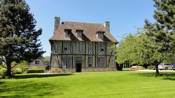 A large, two-story Tudor-style house with a steeply pitched roof, multiple chimneys, and a symmetrical facade with evenly spaced windows.
