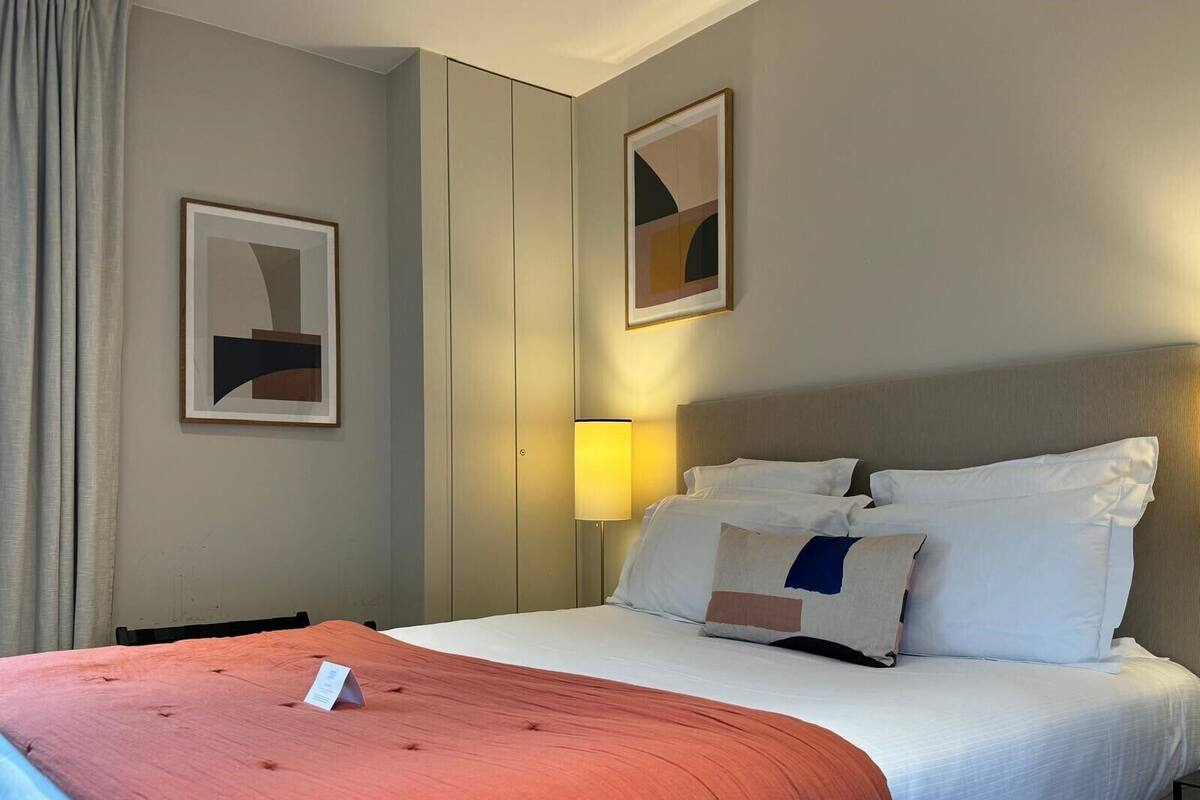 Et hotelværelse med en seng, et natbord, en lampe og to billeder hængende på væggen.