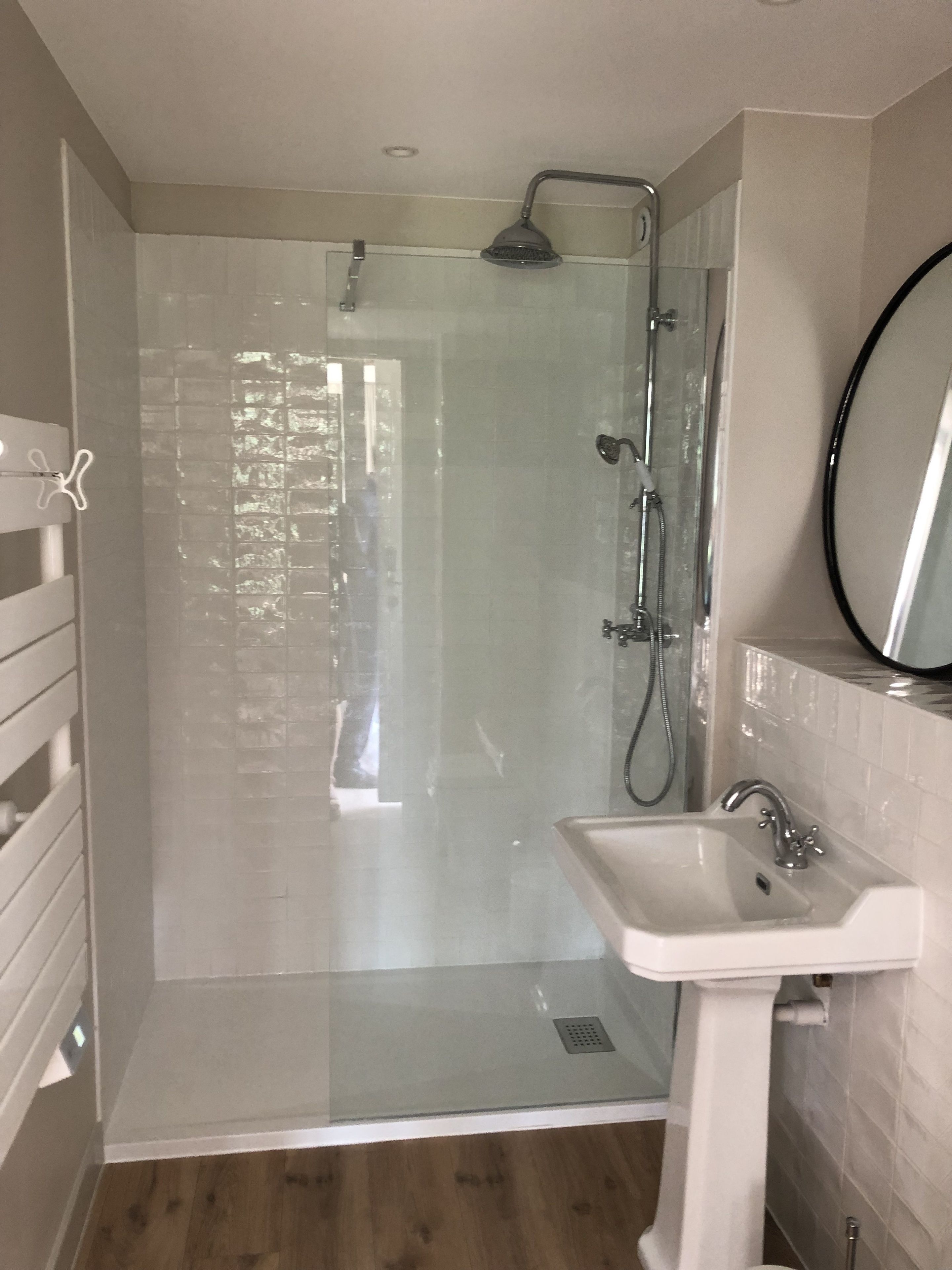 A modern bathroom with a glass shower enclosure, a white sink, and a mirror.