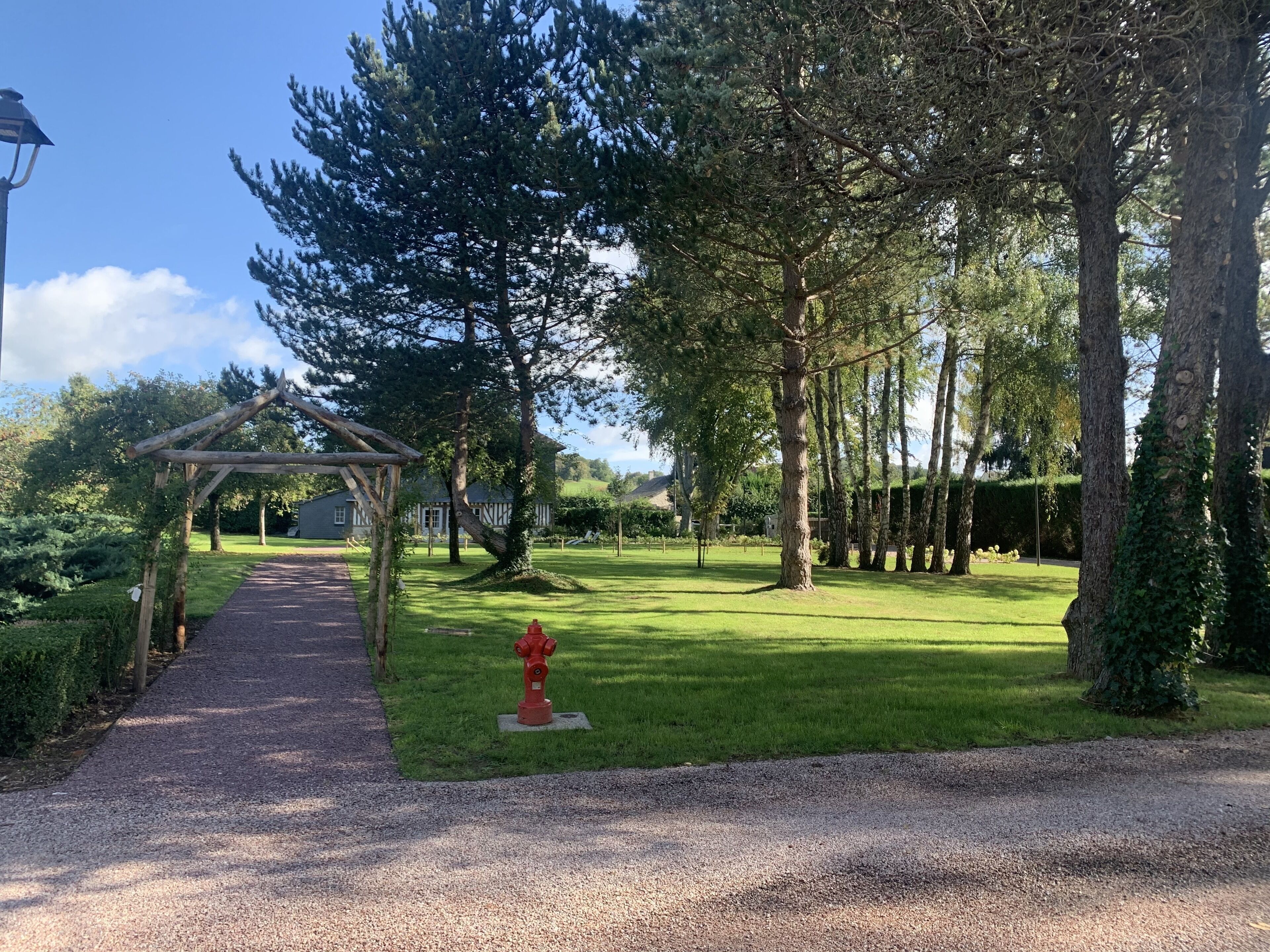 A gravel path leading to a wooden pergola with a clear view of a grassy area and trees.