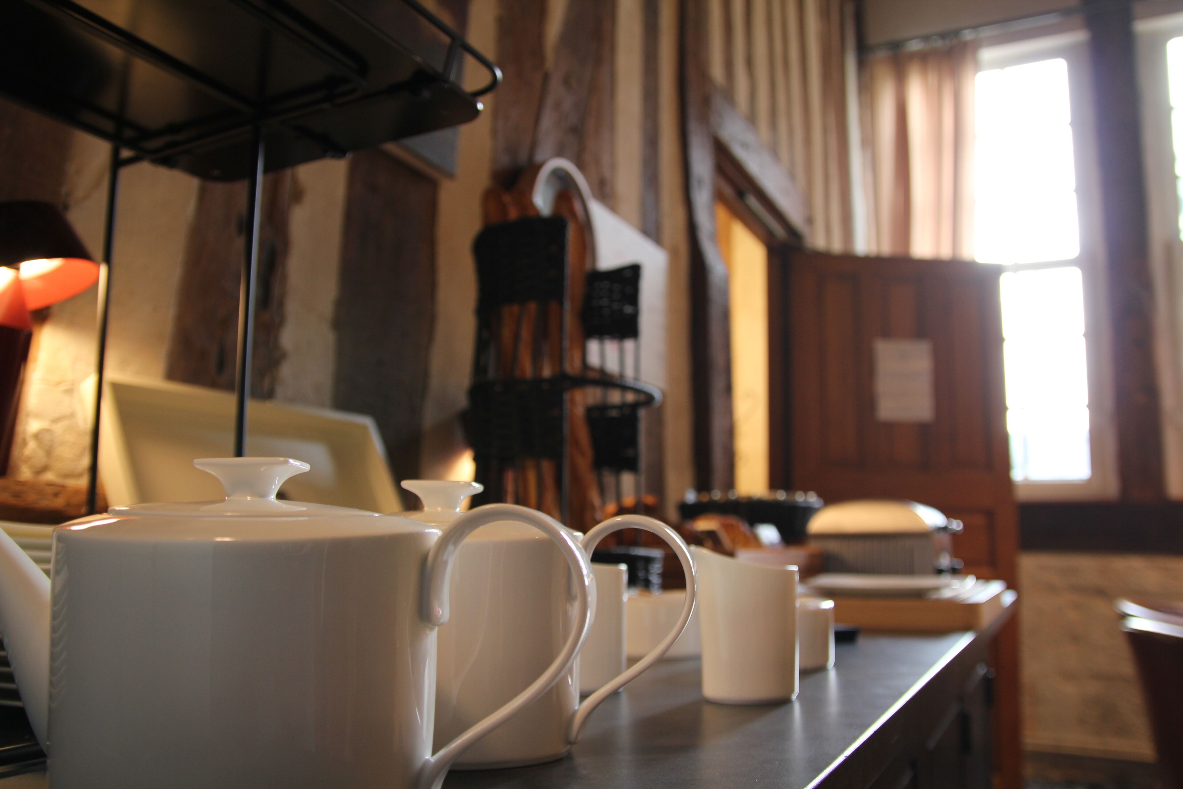 Un coin cuisine avec de la vaisselle en céramique blanche, comprenant une bouilloire, une théière et des tasses, disposée sur un plan de travail.