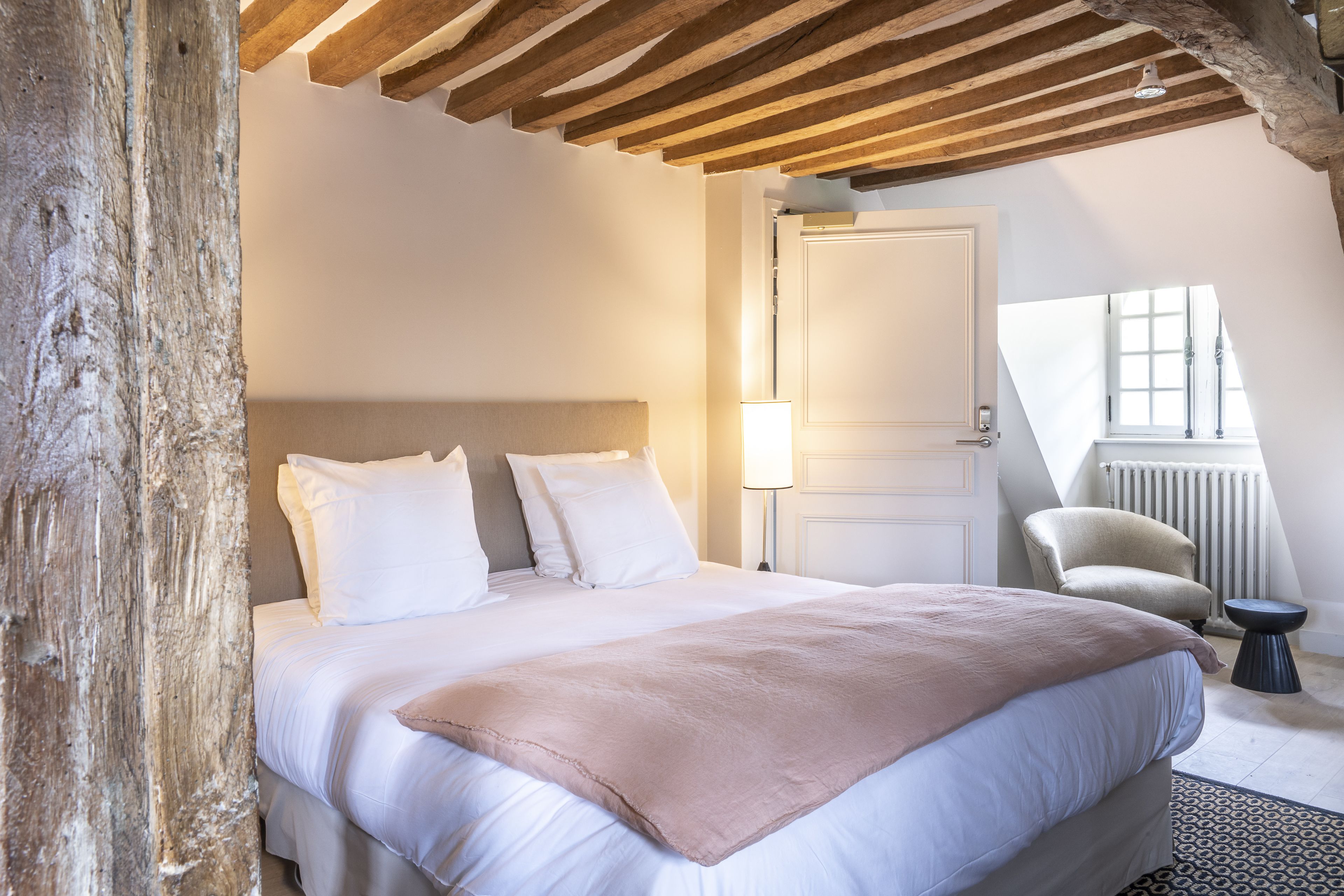 Un dormitorio con una cama grande, techo de madera, una silla y una ventana.