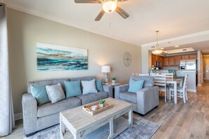 A modern living room with a grey sofa, a wooden coffee table, and a painting of a seascape. A ceiling fan and pendant light are visible.