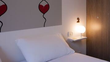 Una cama bien tendida con sábanas blancas, una mesita de noche con una lámpara, y una pared con el número '2' y diseños con forma de corazón.
