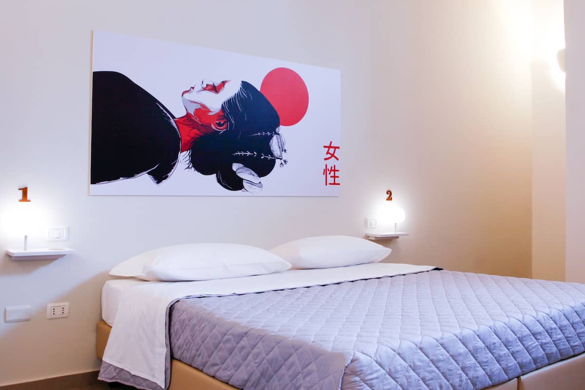 A bedroom with a bed, white pillows, a quilted duvet, a wall-mounted artwork, and two bedside lamps.