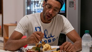A person seated at a table with a plate of food, a water bottle, and a vending machine in the background. - Lobby Collective Hostel (Lecce)