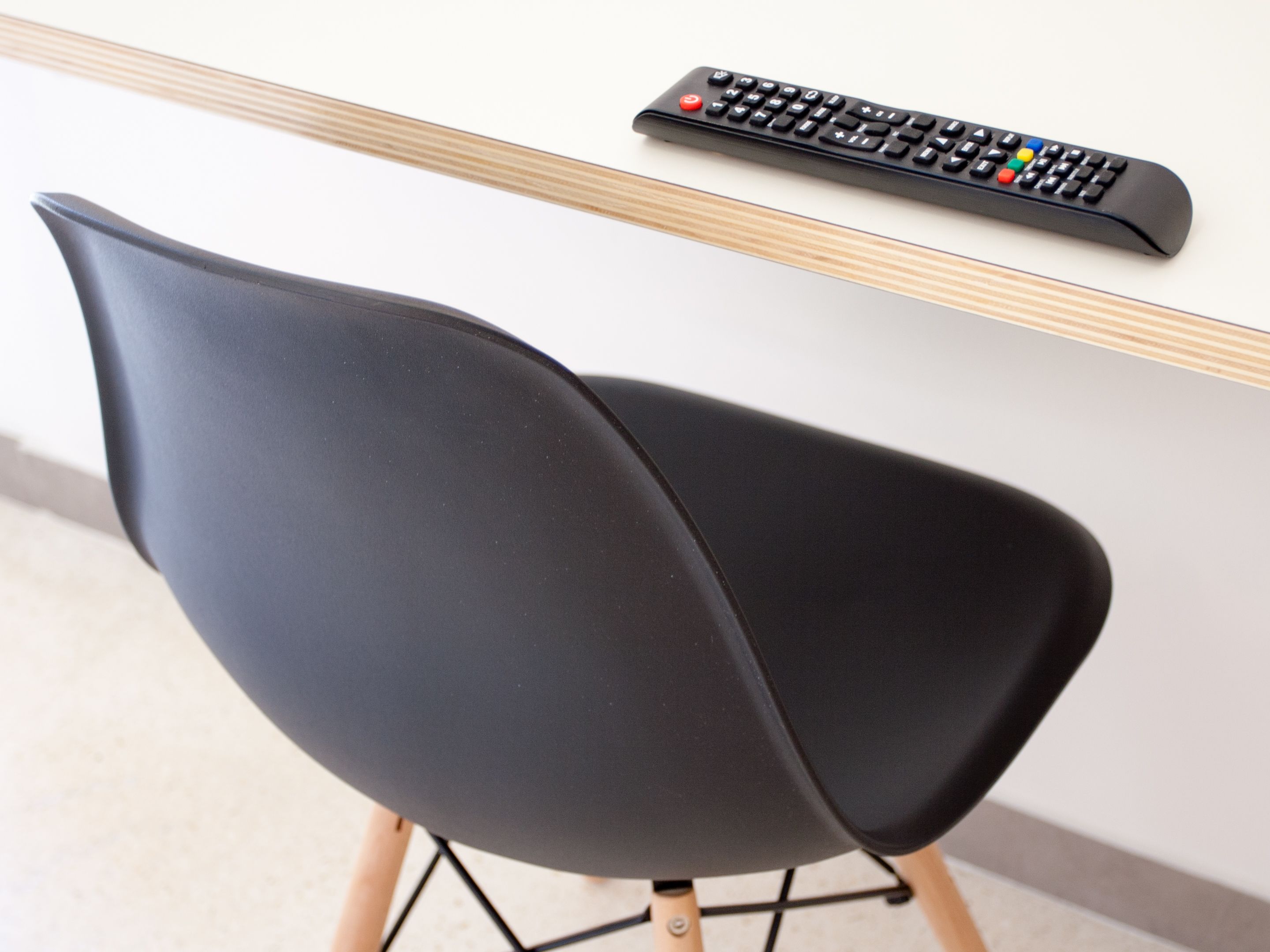 A modern chair with a sleek black design, positioned next to a wooden-framed table with a remote control on it.