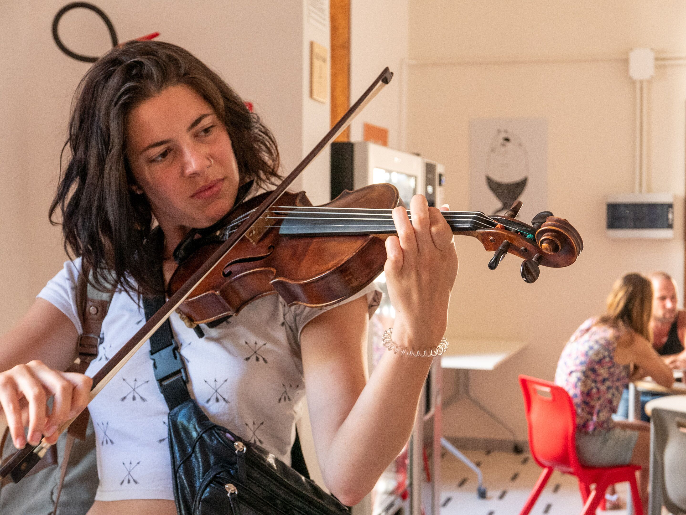 Una persona tocando el violín en una habitación con una pizarra y una silla roja.