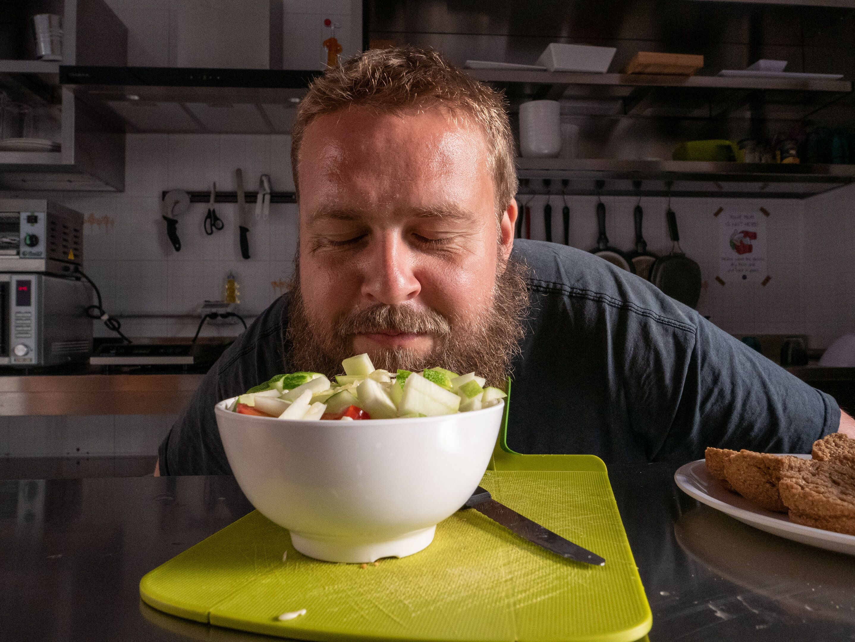 Une personne se trouve dans une cuisine, devant une planche à découper verte sur laquelle se trouve un bol de nourriture.