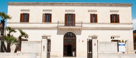 Un bâtiment à deux étages doté d’une façade symétrique, d’une entrée centrale avec une porte en arc de cercle et d’un balcon à l’étage supérieur.