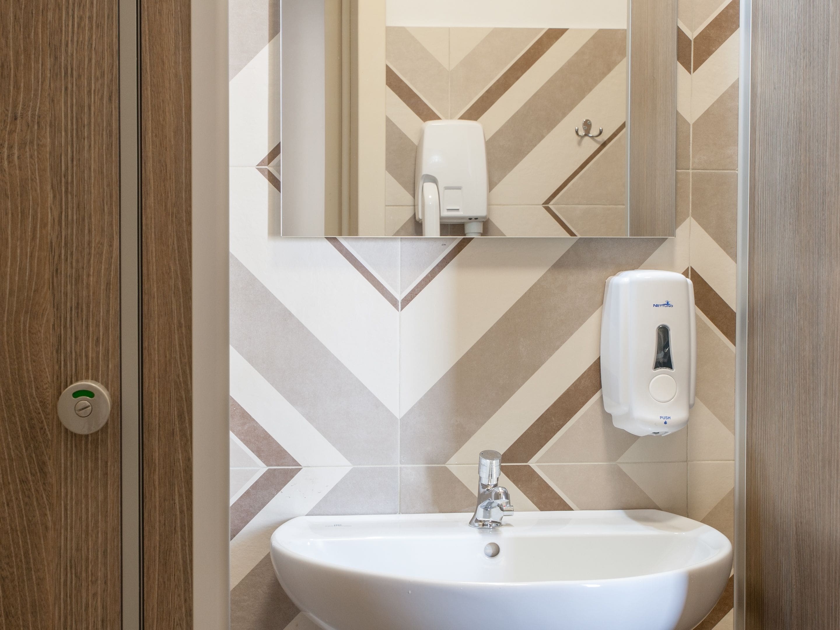 Un bagno con un lavandino bianco, uno specchio e un erogatore di sapone.