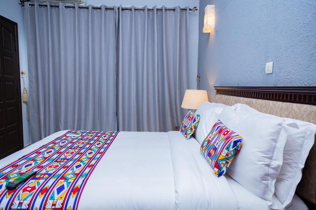 Une chambre d’hôtel avec un lit, des rideaux, une lampe et un luminaire fixé au mur.