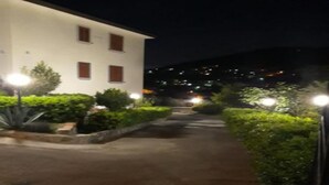 Vista nocturna de un edificio con un sendero pavimentado y abundante vegetación.