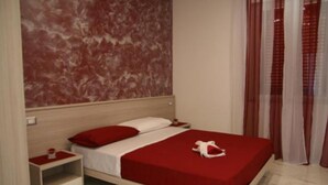 Una cama bien hecha con ropa de cama roja, una mesita de noche con una bandeja roja, y una pared con diseño de mármol.