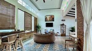 Ruime kamer met een hoge plafond, een centraal zithoek en een eethoek met rieten meubels.