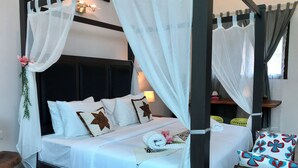 Een bed met hemelbed, wit beddengoed en decoratieve kussens.