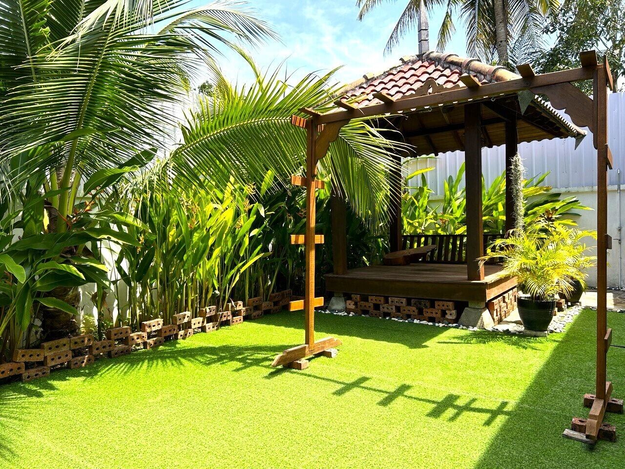 Une pergola en bois, surmontée d’un toit en tuiles, entourée d’une végétation luxuriante et d’une pelouse bien entretenue.