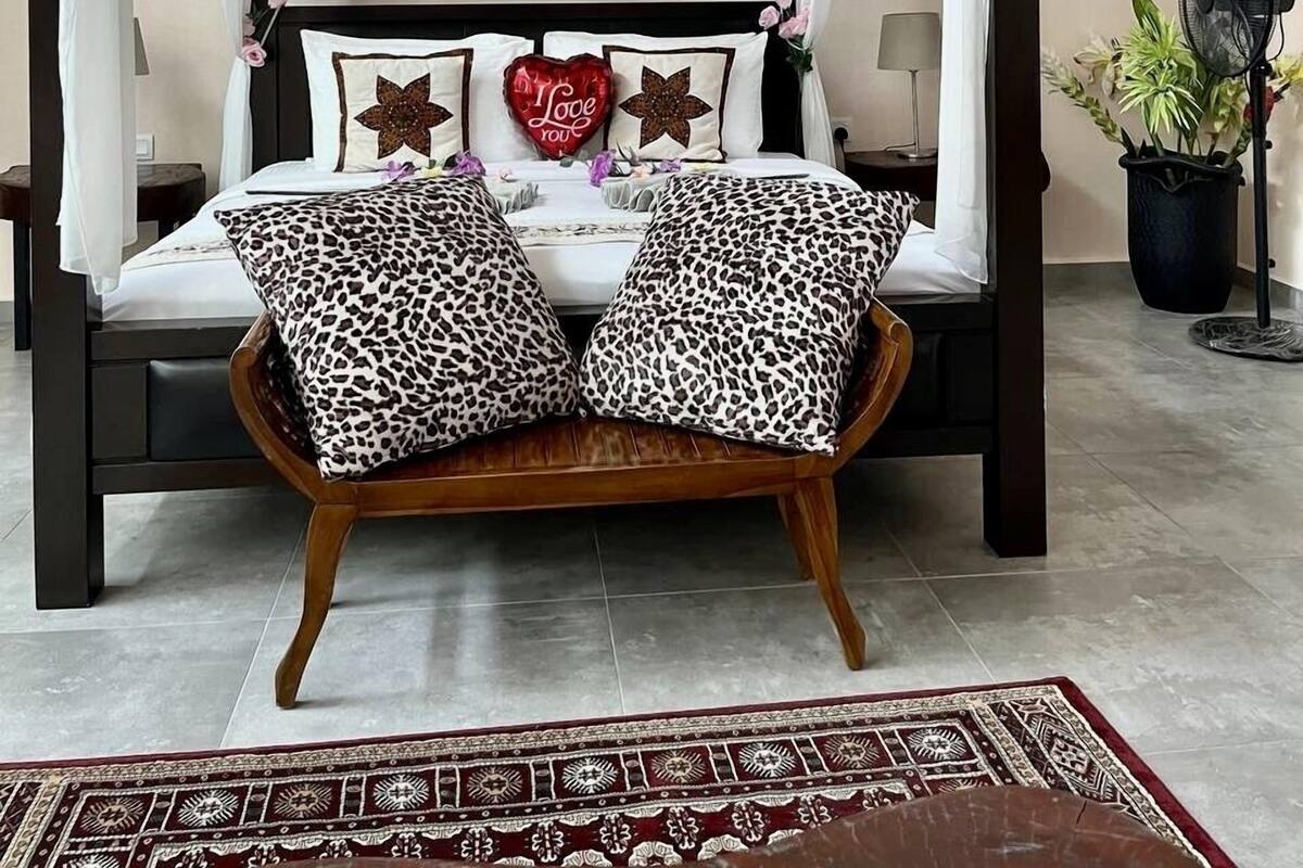 A four-poster canopy bed with a wooden frame, white bedding, and leopard print pillows.