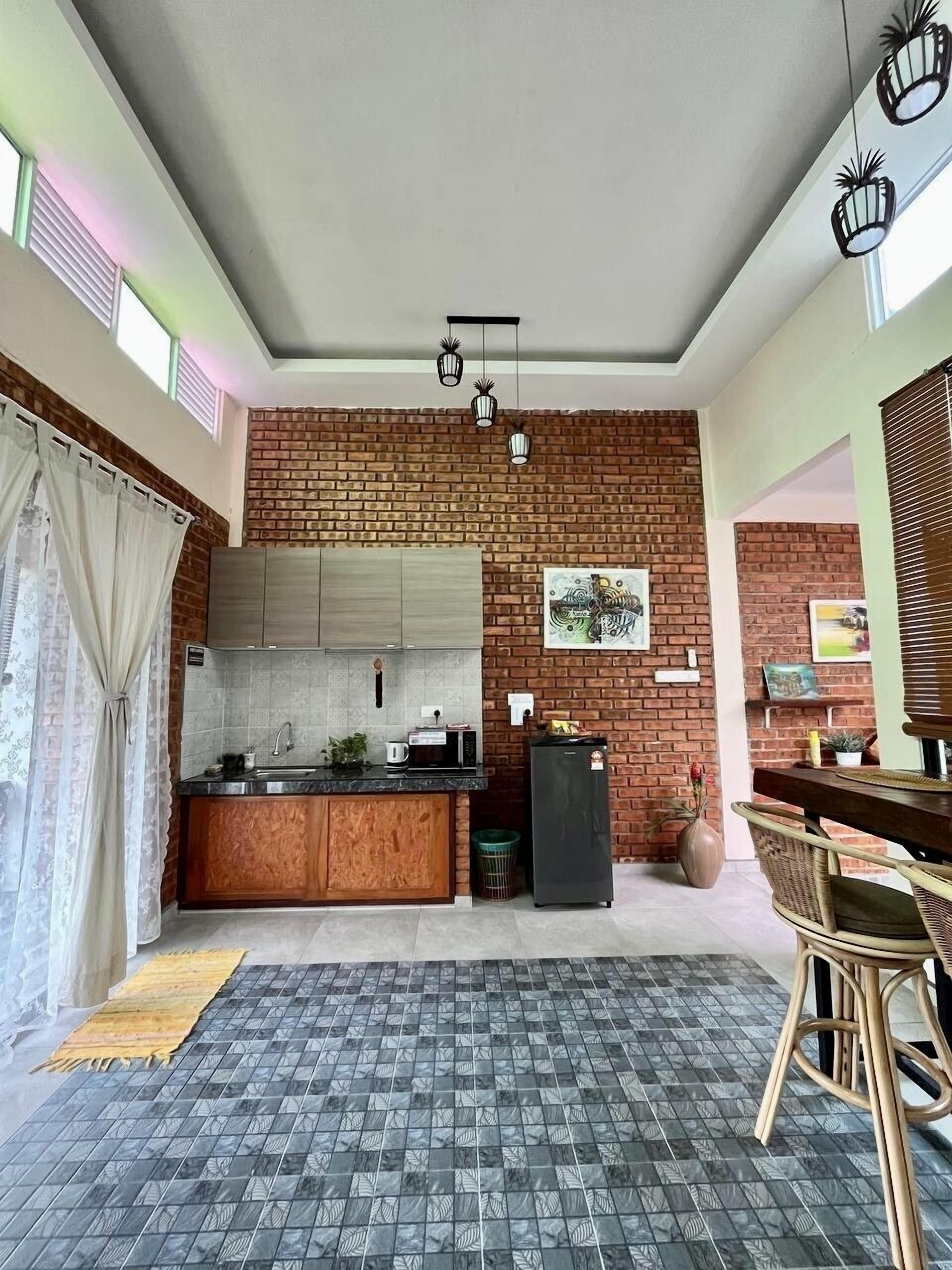 A kitchen with a brick wall, wooden cabinets, a black refrigerator, and a dining area with wicker chairs.