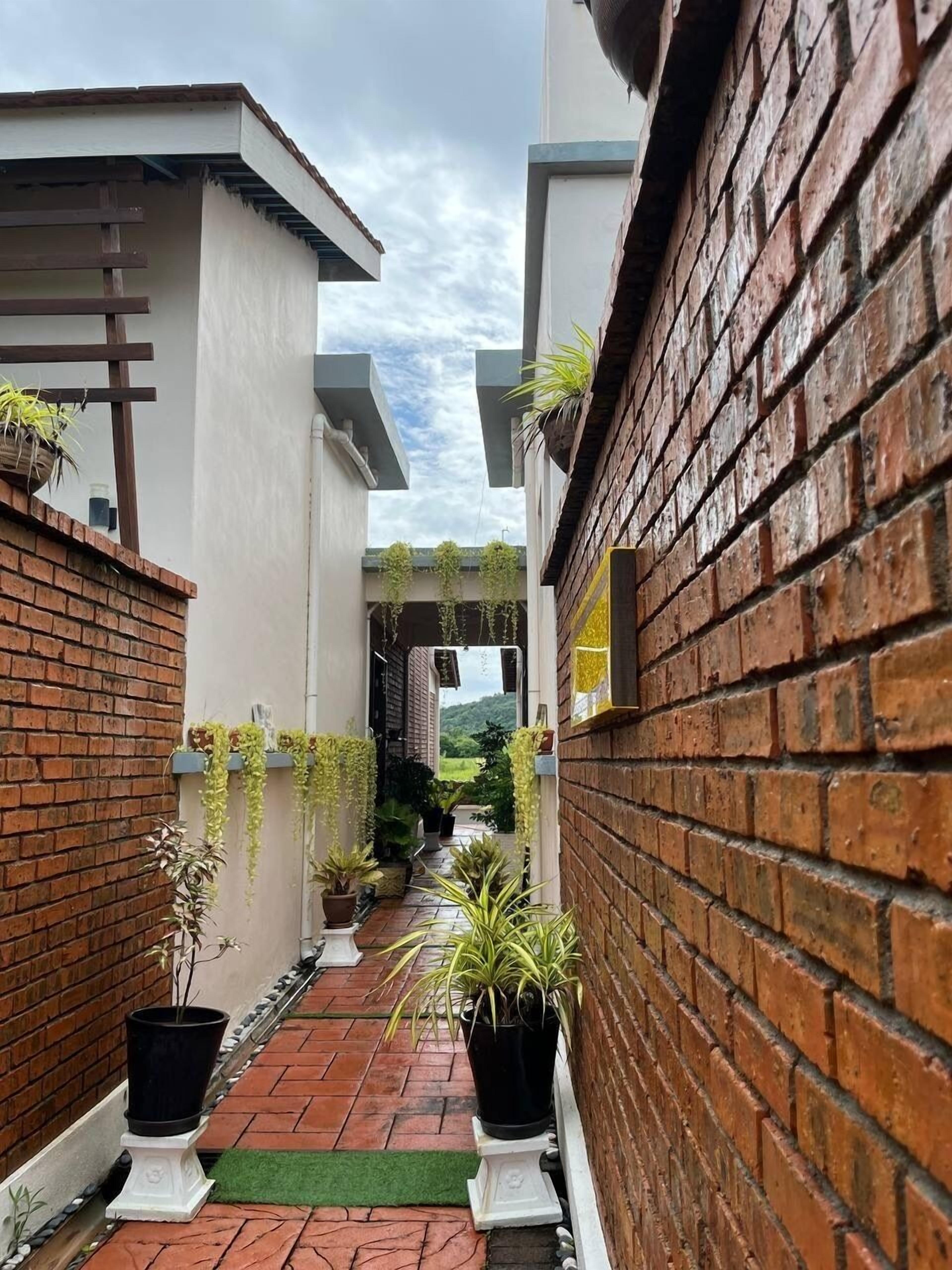 Un étroit sentier bordé de murs de briques et d’immeubles blancs, qui mène à une entrée abritée.