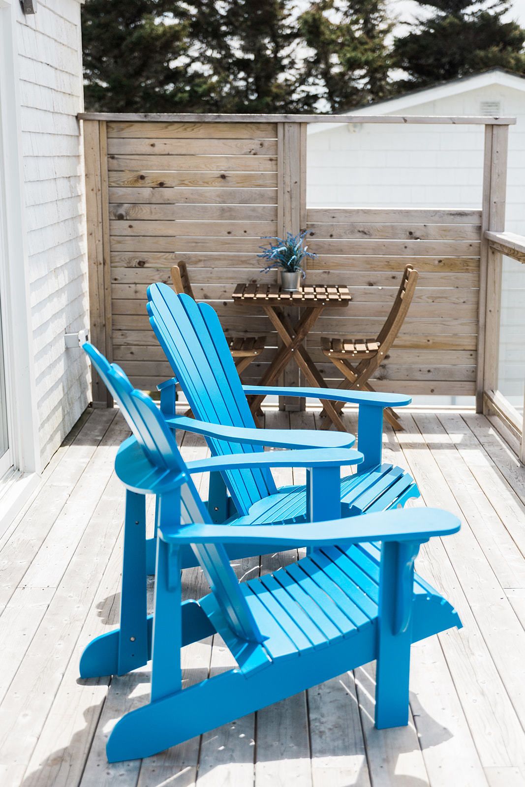 Un patio in legno con due poltrone Adirondack blu e un tavolino in legno con una pianta in vaso.
