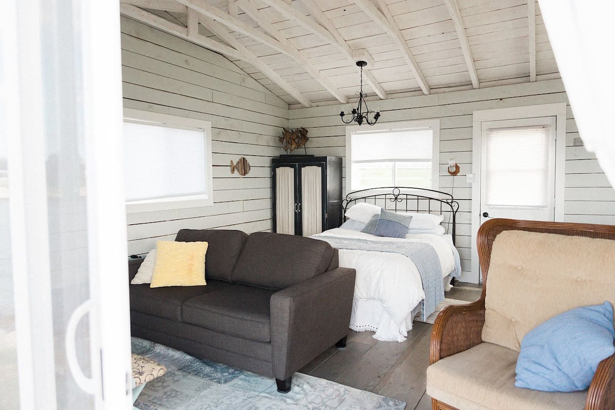 A cozy bedroom with a bed, a dark sofa, a chair, and a wardrobe.