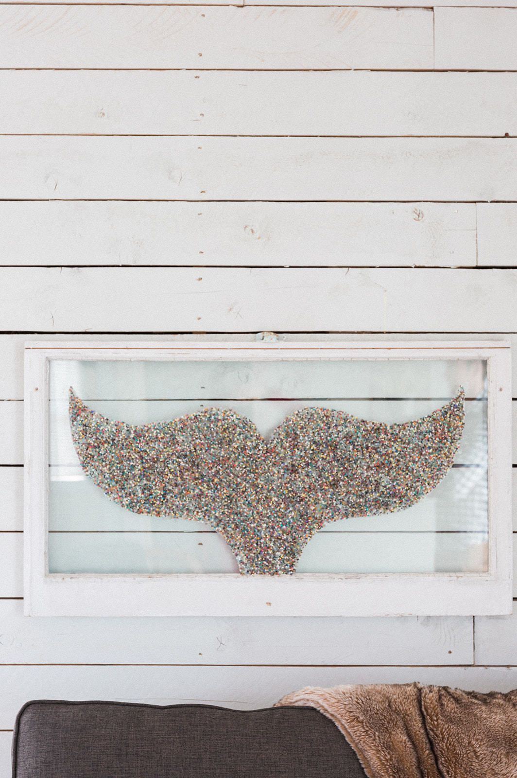 Una obra de arte enmarcada de una mariposa sobre una pared de madera blanca.