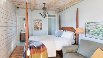 Un dormitorio con cama de dos plazas, techo de madera, candelabro, cuadro de peces, sofá y alfombra estampada.