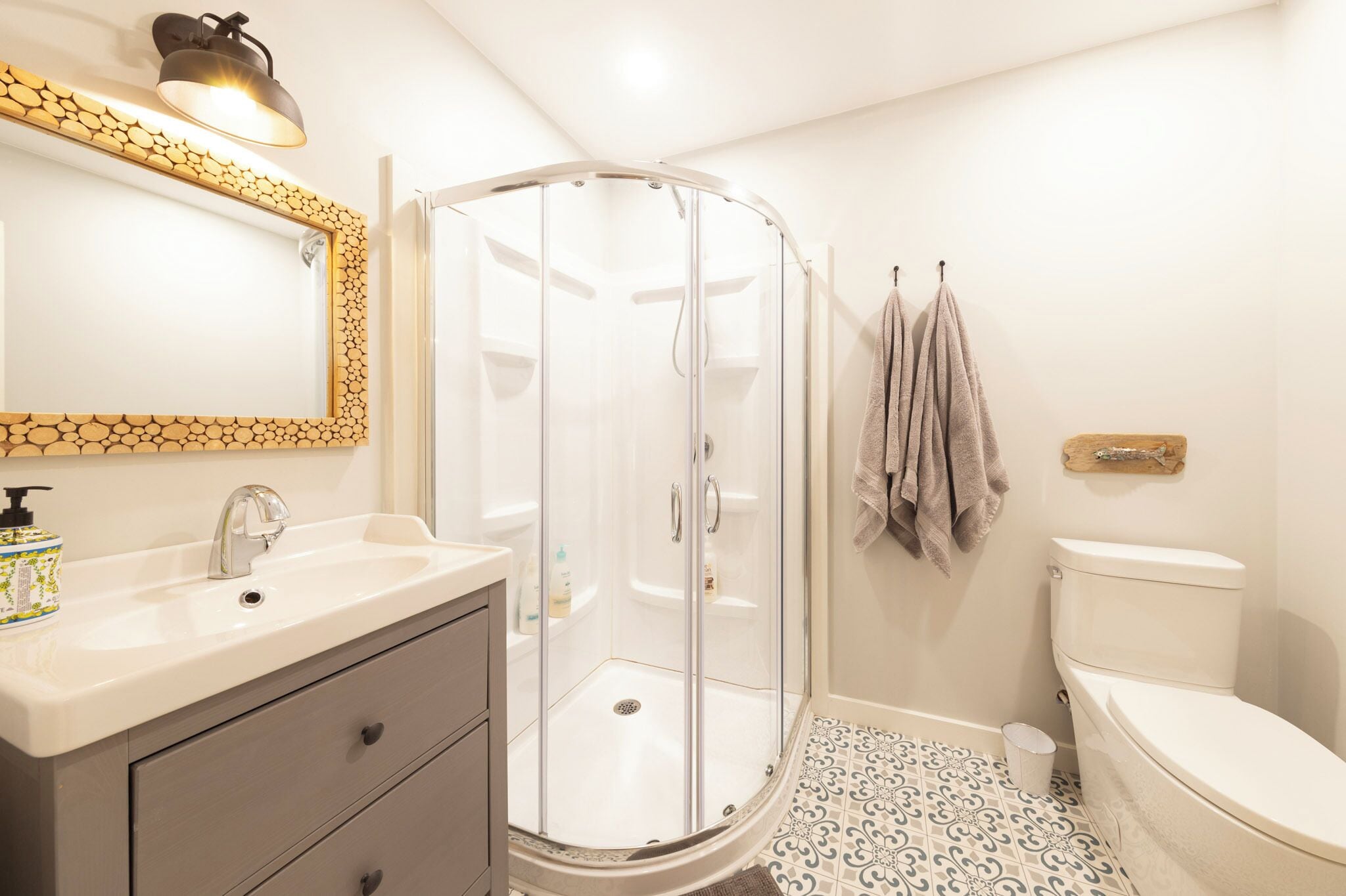 Un baño con ducha vidriada, lavamanos con dispensador de jabón y un inodoro.