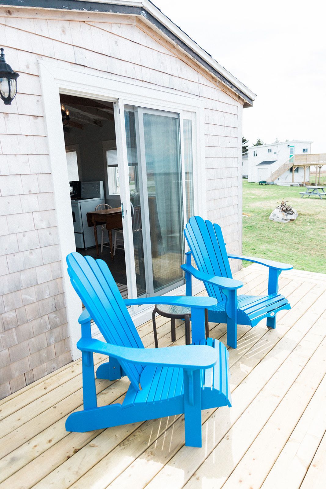 Een houten terras met twee blauwe Adirondack-stoelen en een kleine tafel.