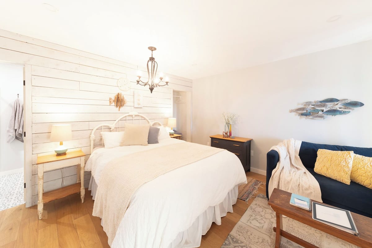 A bedroom with a large bed, bedside tables, a dresser, a chandelier, a sofa, and a wall decoration.