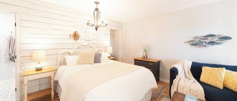 A bedroom with a large bed, bedside tables, a dresser, a chandelier, a sofa, and a wall decoration.