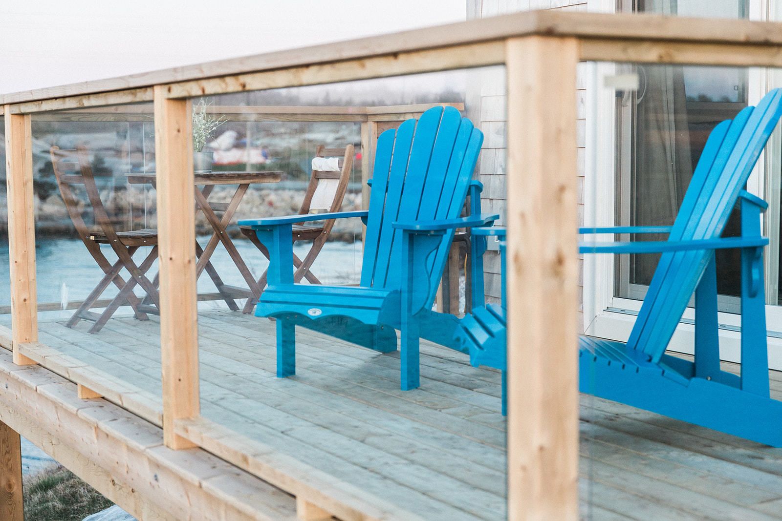 A wooden deck with blue Adirondack chairs and a wooden table.