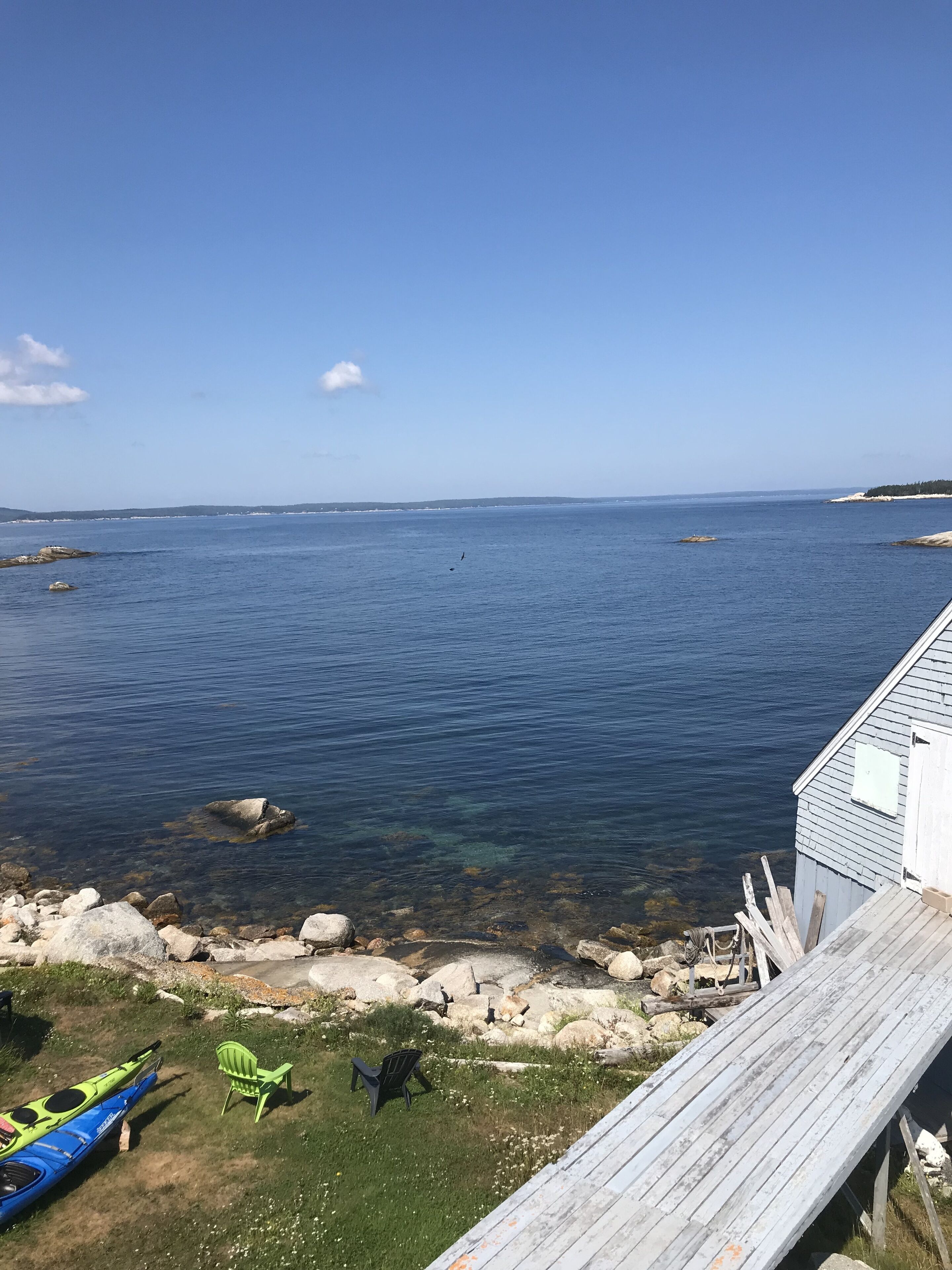 Une terrasse en bois surplombant une étendue d’eau calme, avec des kayaks et des chaises sur la rive.