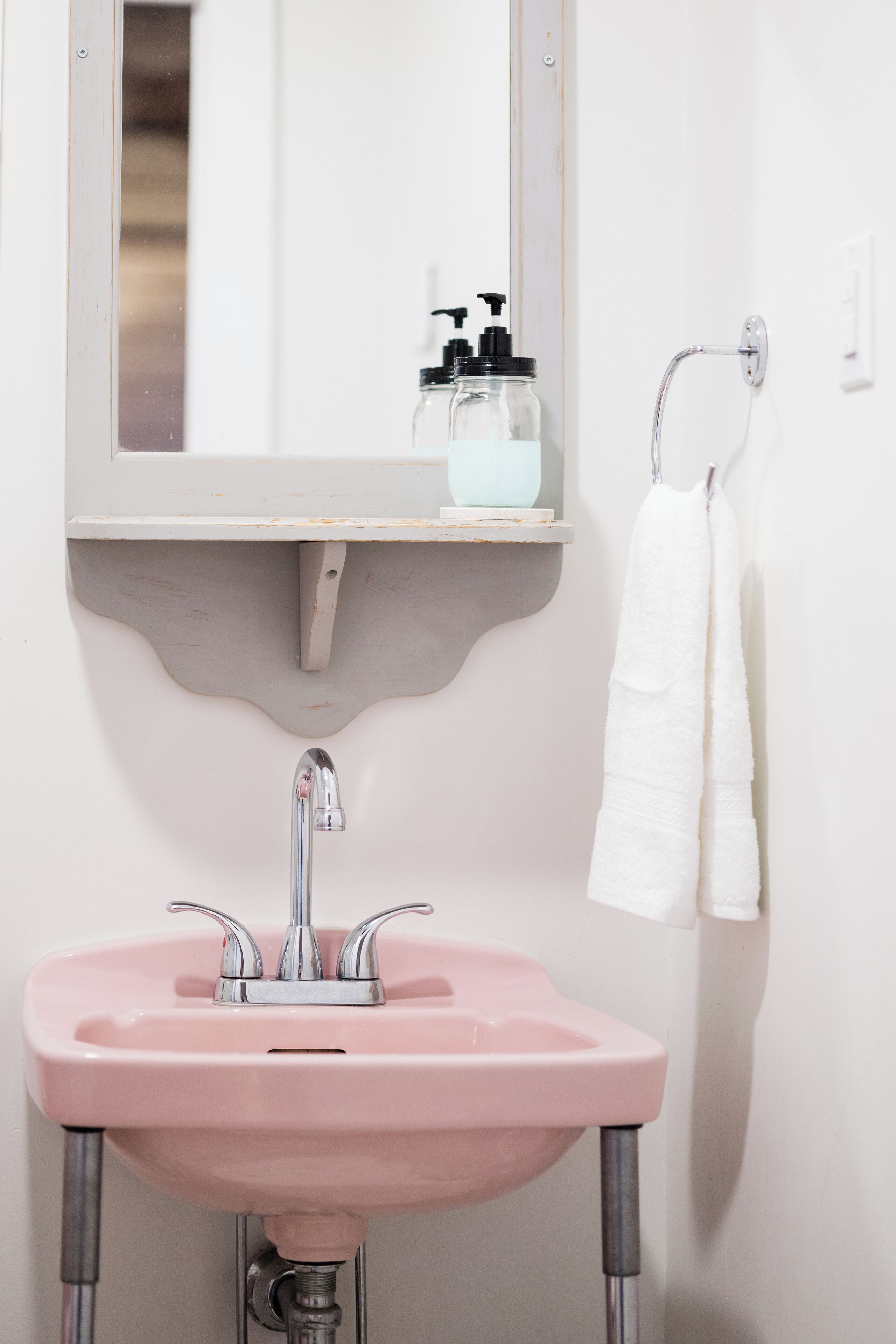 Ein Badezimmer mit einem rosa Waschbecken, einem Spiegel, einem Handtuchhalter und einer Seifenspender.